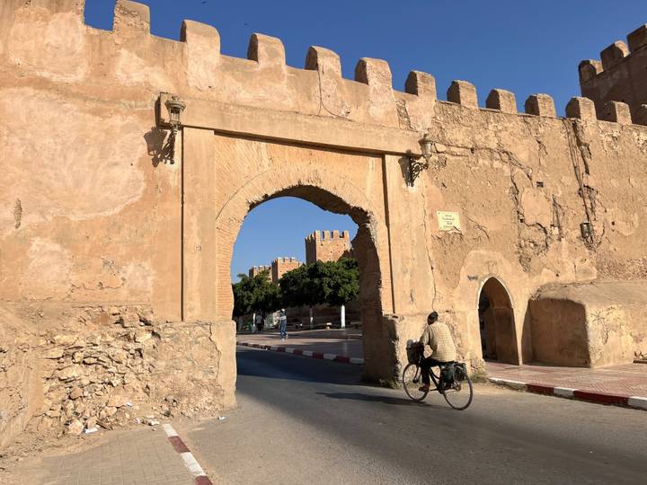 Cyclist passes through an ancient adobe archway with crenellations and textured stonework.