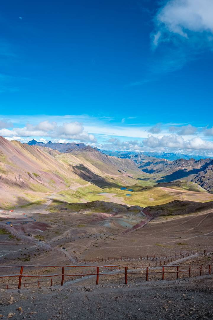 High-altitude panorama with emerald ponds and pastel mountains under bright blue sky.