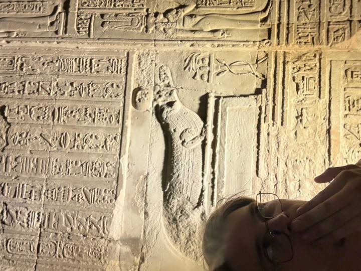 Close-up selfie beside illuminated ancient Egyptian hieroglyphic wall relief showing a crocodile figure.