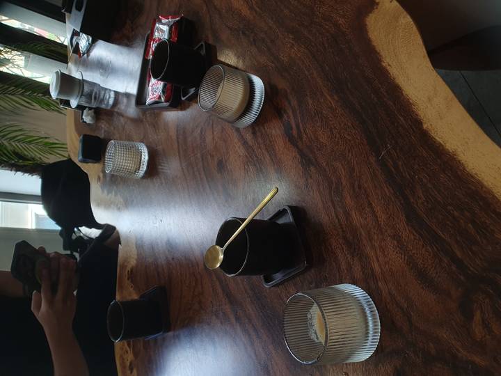 Wooden table with stylish black cups, a gold spoon and minimalistic café setting.