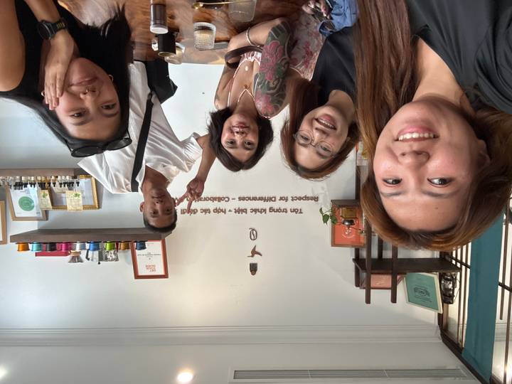 Five smiling travellers posing inside a cozy café with travel mementos on the wall.