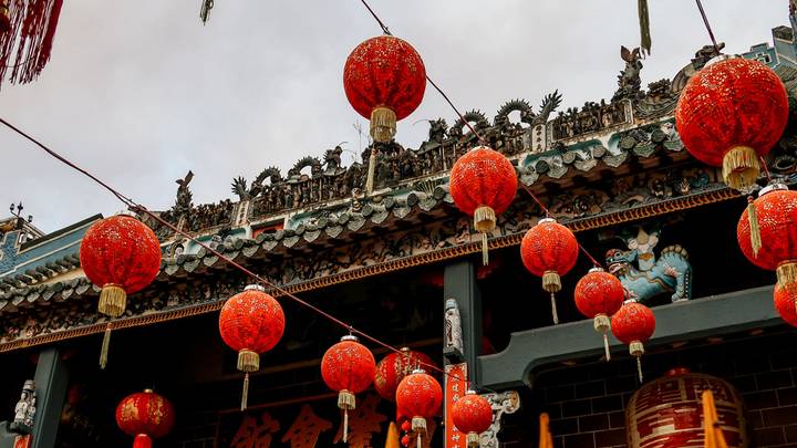 Bright red lanterns strung in front of an ornate temple façade with intricate carvings.