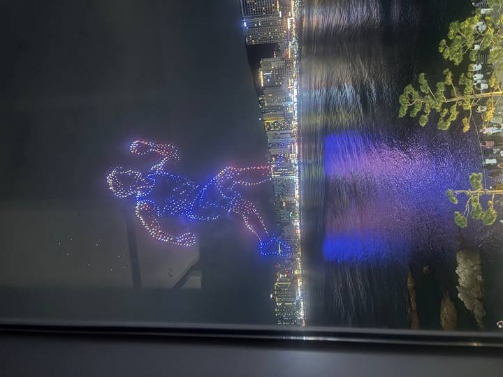Colourful drone light show forming a running figure above Busan’s waterfront skyline at night.