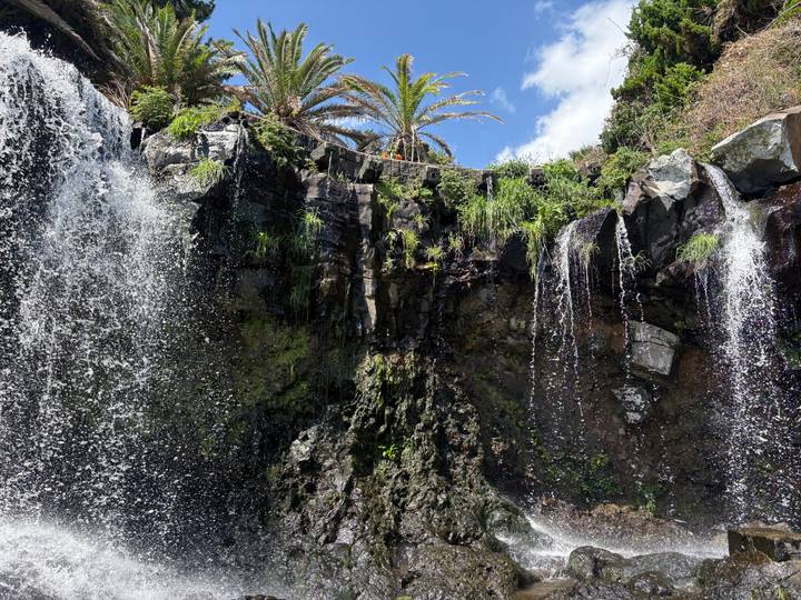 Refreshing multi-tiered waterfall cascading over dark rocks with palm trees overhead.