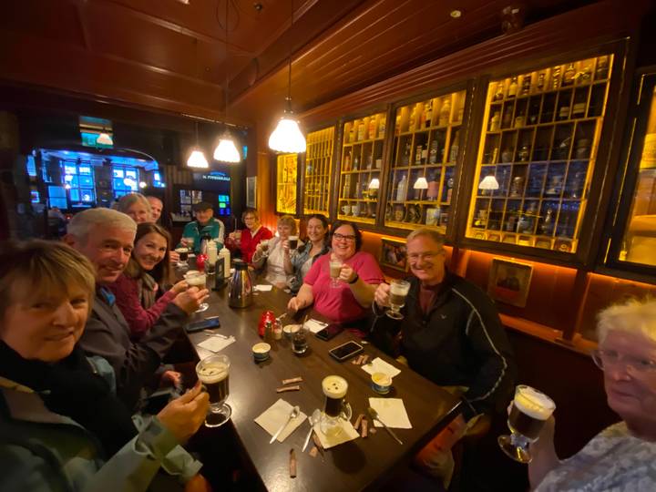 Lively pub interior where travellers raise glasses of Irish coffee around a long wooden table.