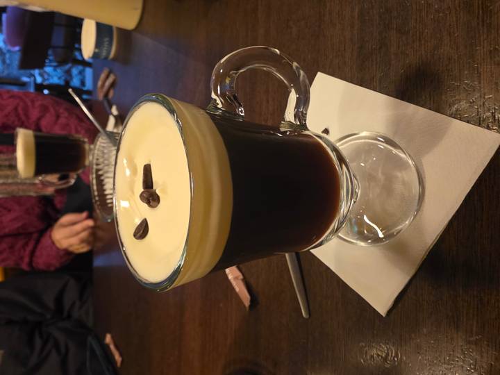 Close-up of creamy Irish coffee garnished with coffee beans in a glass mug on a wooden table.
