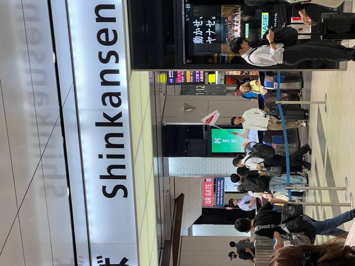 Busy Shinkansen station entrance with travellers queuing beneath a large sign.