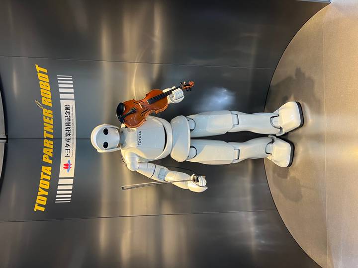 White humanoid Toyota Partner Robot holds a violin inside a modern exhibition space.