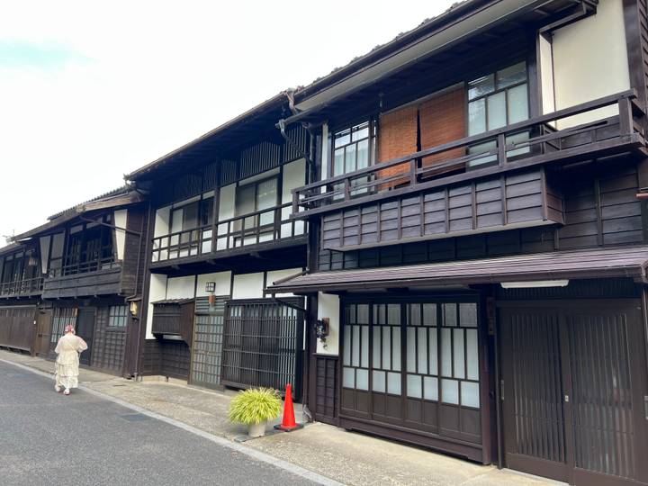 Row of preserved dark-wood machiya townhouses along a quiet street with a kimono-clad walker.