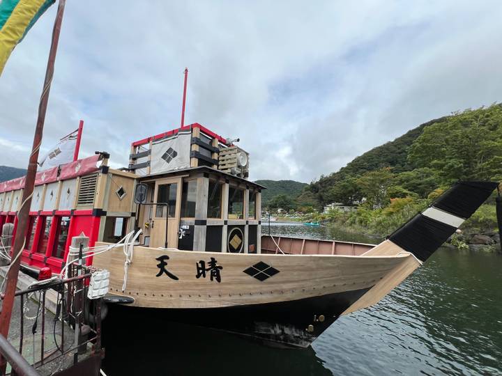 Traditional wooden pleasure boat with bold red accents moored on a lake backed by forested hills.