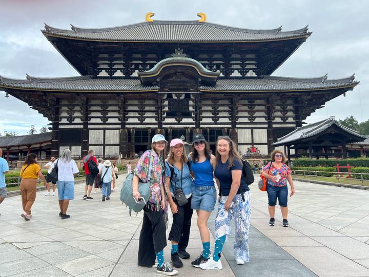 Friends pose happily in front of the grand wooden facade of Todai-ji temple while visitors mill about.
