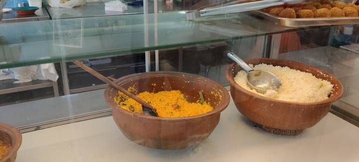Two clay pots of yellow and white rice behind a glass counter inside a casual eatery.