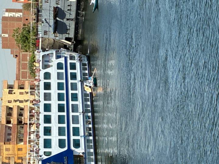 Small rowboat with two men paddling beside a large white Nile cruise ship docked on the river