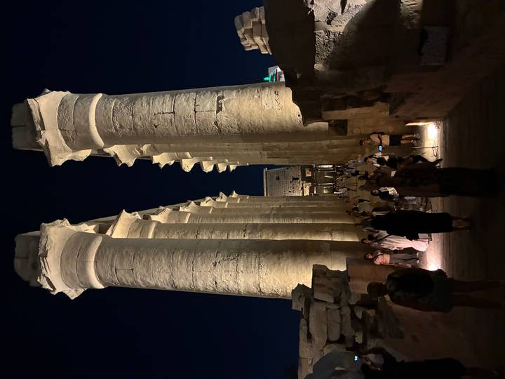 Night view of the illuminated colonnade of Luxor Temple with visitors walking between towering columns