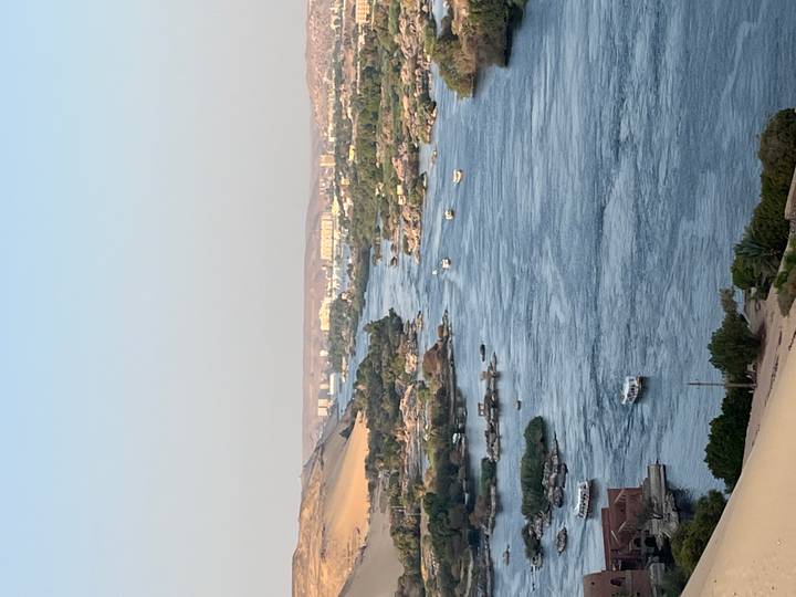 Vertical shot of the Nile River coursing between sandy hills and green islands under clear skies