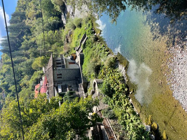 Traditional stone house with red roof beside a clear blue stream in a leafy Greek valley