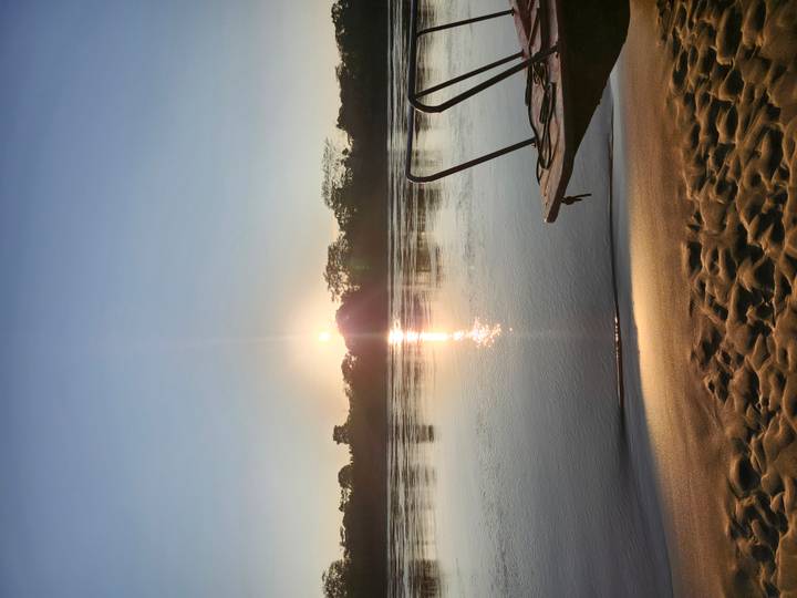Calm dawn on an Amazon sandbar with rising sun reflected in glassy water and a wooden boat ladder