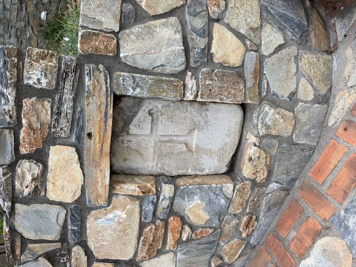 Weathered stone relief with a cross set into a rustic rock wall.