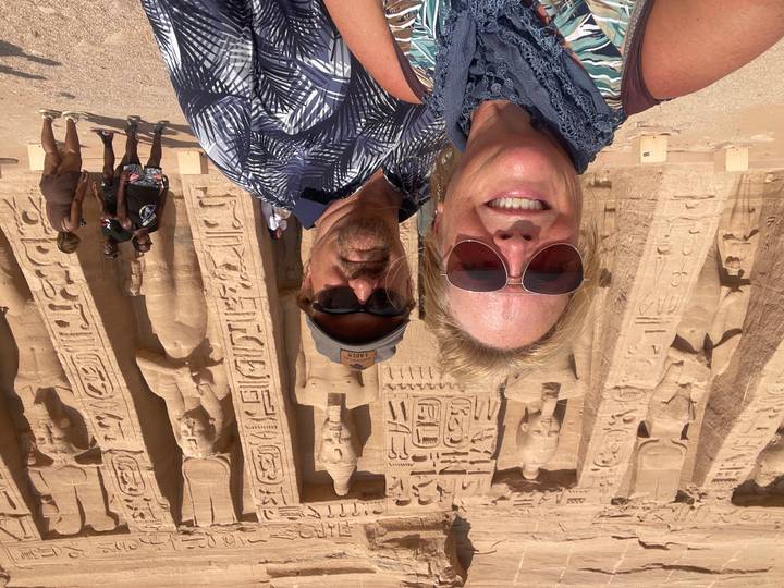 Close-up selfie of a couple in sunglasses at the colossal statues of Abu Simbel under bright desert sun.