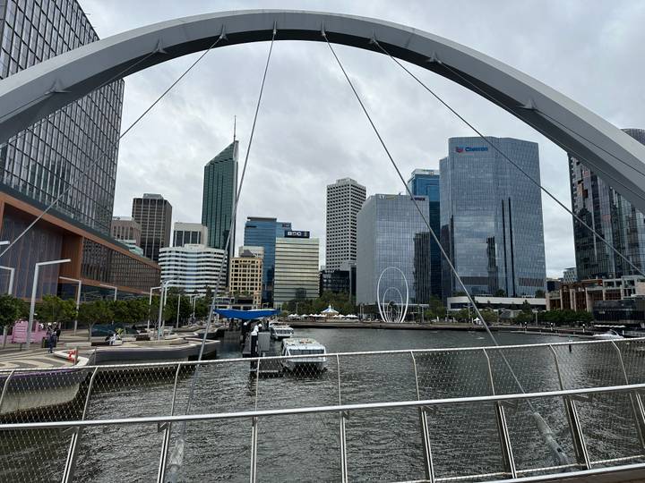 Modern skyline of Perth seen across Elizabeth Quay with boats and curved pedestrian bridge framing the view.