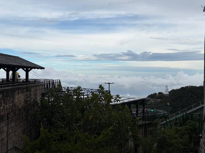 Mountain viewpoint above a sea of clouds with distant structures and lush greenery in Ba Na Hills area.