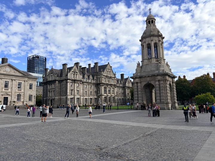 Courtyard scene at Trinity College Dublin with the Campanile tower and historic stone buildings under a blue-sky dotted with clouds.