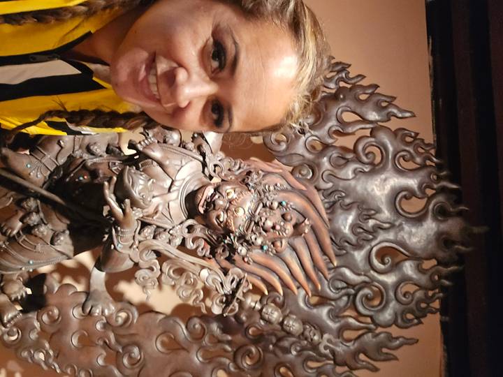 Woman takes a selfie beside an intricate fiery metal deity statue inside a museum or temple.