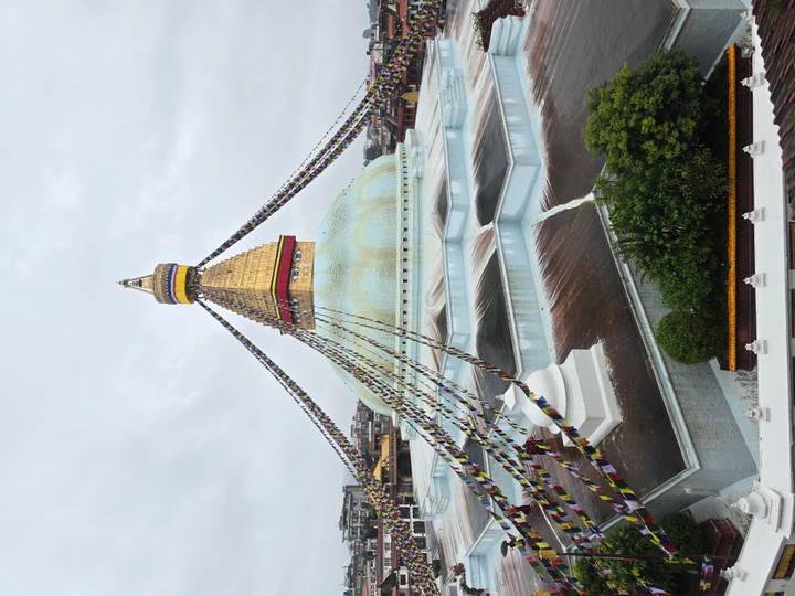 The golden spire and white dome of Boudhanath Stupa draped with colorful prayer flags dominate the Kathmandu skyline.