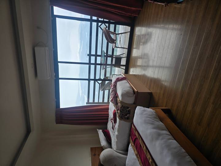 Bright hotel room with twin beds, wooden floors and a balcony overlooking distant mountains and clouds.