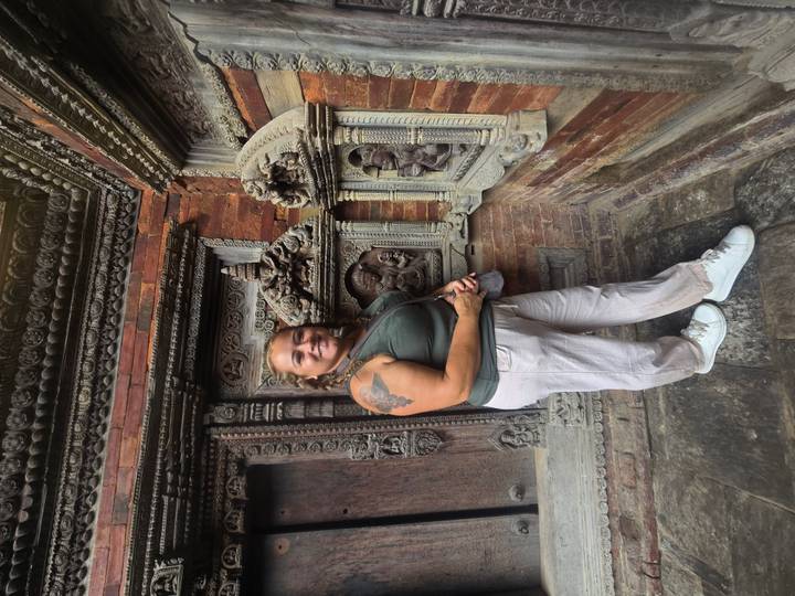 Female traveller poses beside intricate brick and wood carvings on an ancient temple wall.