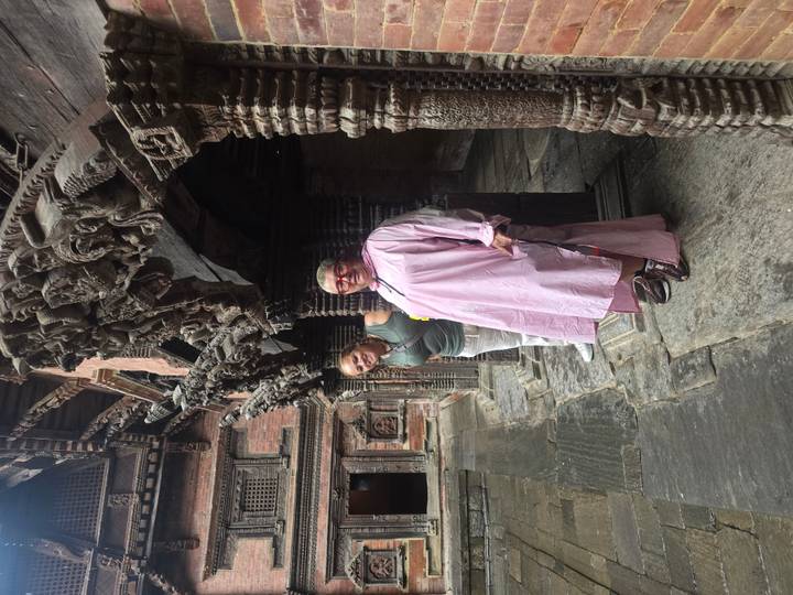 Two women explore an ornately carved wooden arcade inside an ancient palace courtyard.