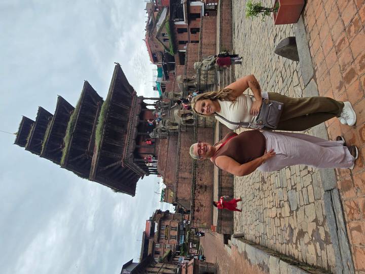 Two women pose in front of a tall tiered temple and stone guardians in an historic square.