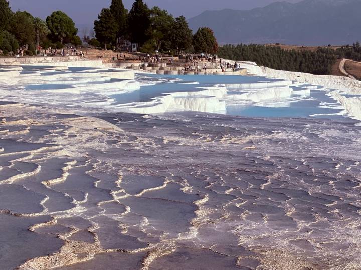 white travertine terraces of Pamukkale with shallow turquoise pools and visitors walking