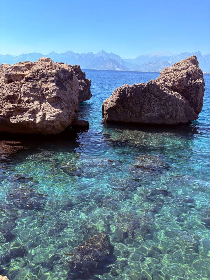 Crystal-clear turquoise sea water glistening around large coastal rocks.
