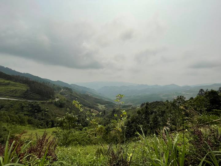A wide, misty view over lush green valleys and layered mountains beneath a cloudy sky.