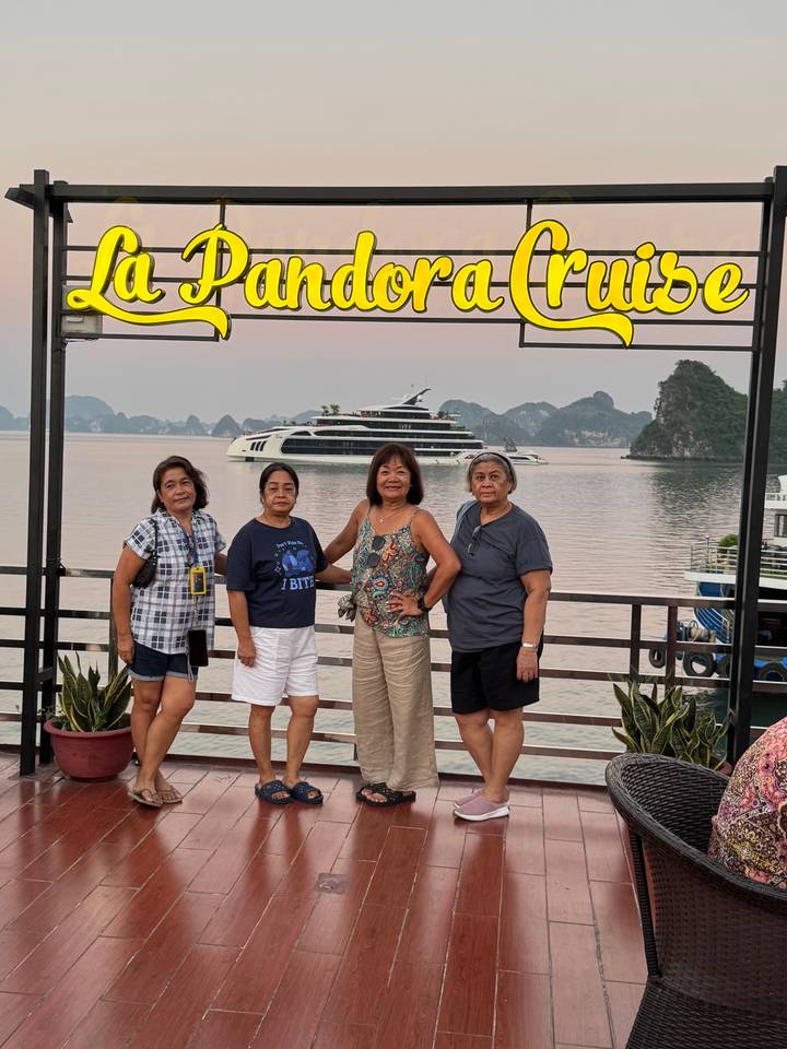 Four women posing on a boat deck with a luxury cruise ship and limestone karsts in the background.