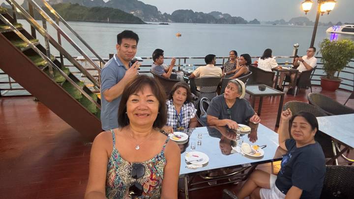 Travelers dining on an open deck overlooking calm bay waters at dusk.