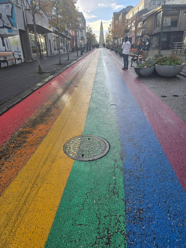 Rain-soaked rainbow painted street in Reykjavik featuring a circular manhole cover at centre.