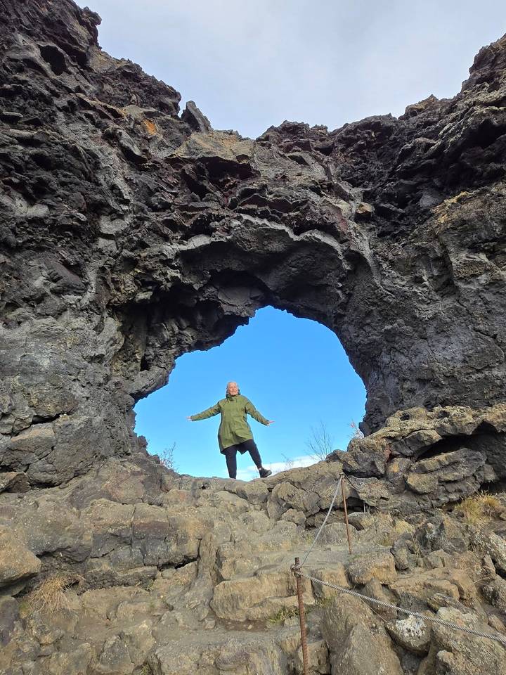 Traveller poses triumphantly beneath a natural lava arch against a vivid blue Icelandic sky.