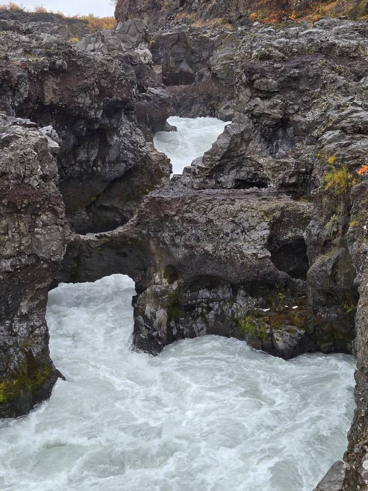 Eroded volcanic rock formations rise amid whitewater rapids carving through a rugged canyon.