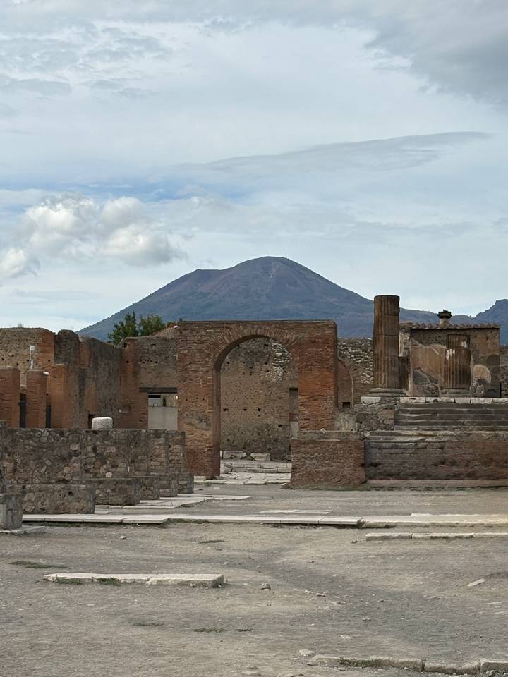 Ancient brick arches and columns of Pompeii with Mount Vesuvius looming in the background.