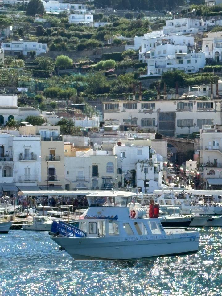 Busy waterfront town with pastel buildings and ferry docks on a hazy Mediterranean morning.