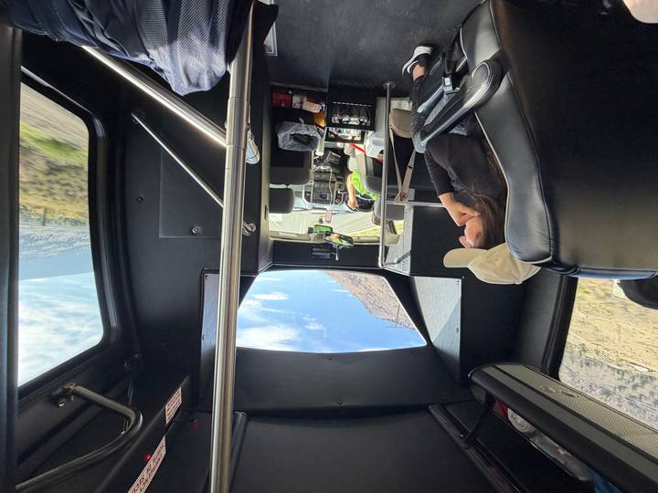 Passengers seated in a tour bus gaze forward as the vehicle winds along a scenic highway.
