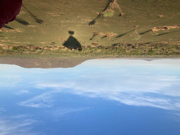 Wide savannah panorama with distant mesas and shadow of a hot-air balloon on the ground.