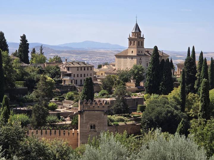 Scenic view over Alhambra gardens, tower and distant mountains under clear sky.