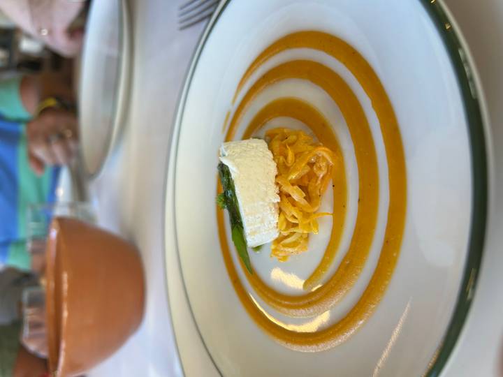 Gourmet plated appetizer with spiral sauce, shredded vegetables and cheese round.