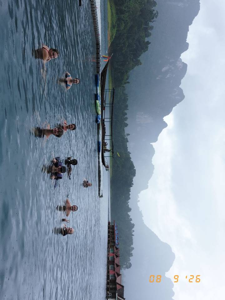 Travellers enjoy a refreshing swim in a misty lake beneath limestone cliffs.