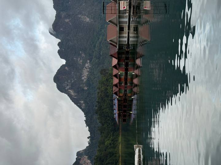 Floating wooden bungalows reflect in the calm emerald waters of a mountain lake at dawn.