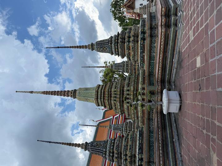 Ornate spires of Wat Pho rising against a partly cloudy sky inside a Thai temple courtyard.
