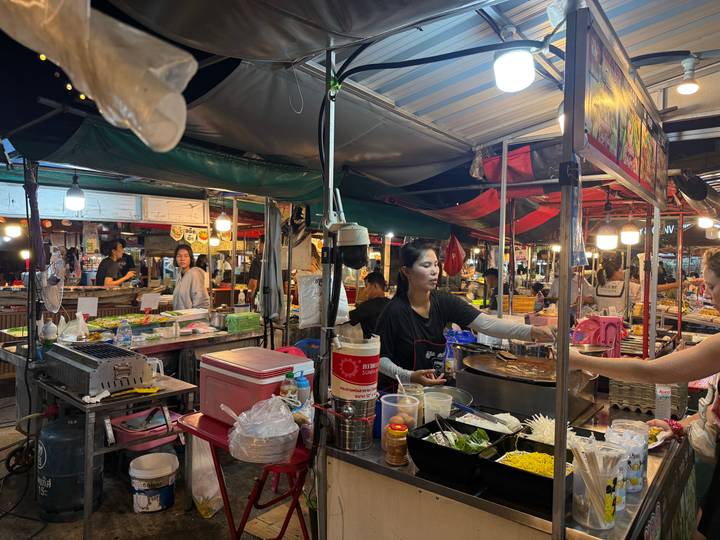 Bustling Thai night market food stall where vendors prepare colorful dishes under bright lights.